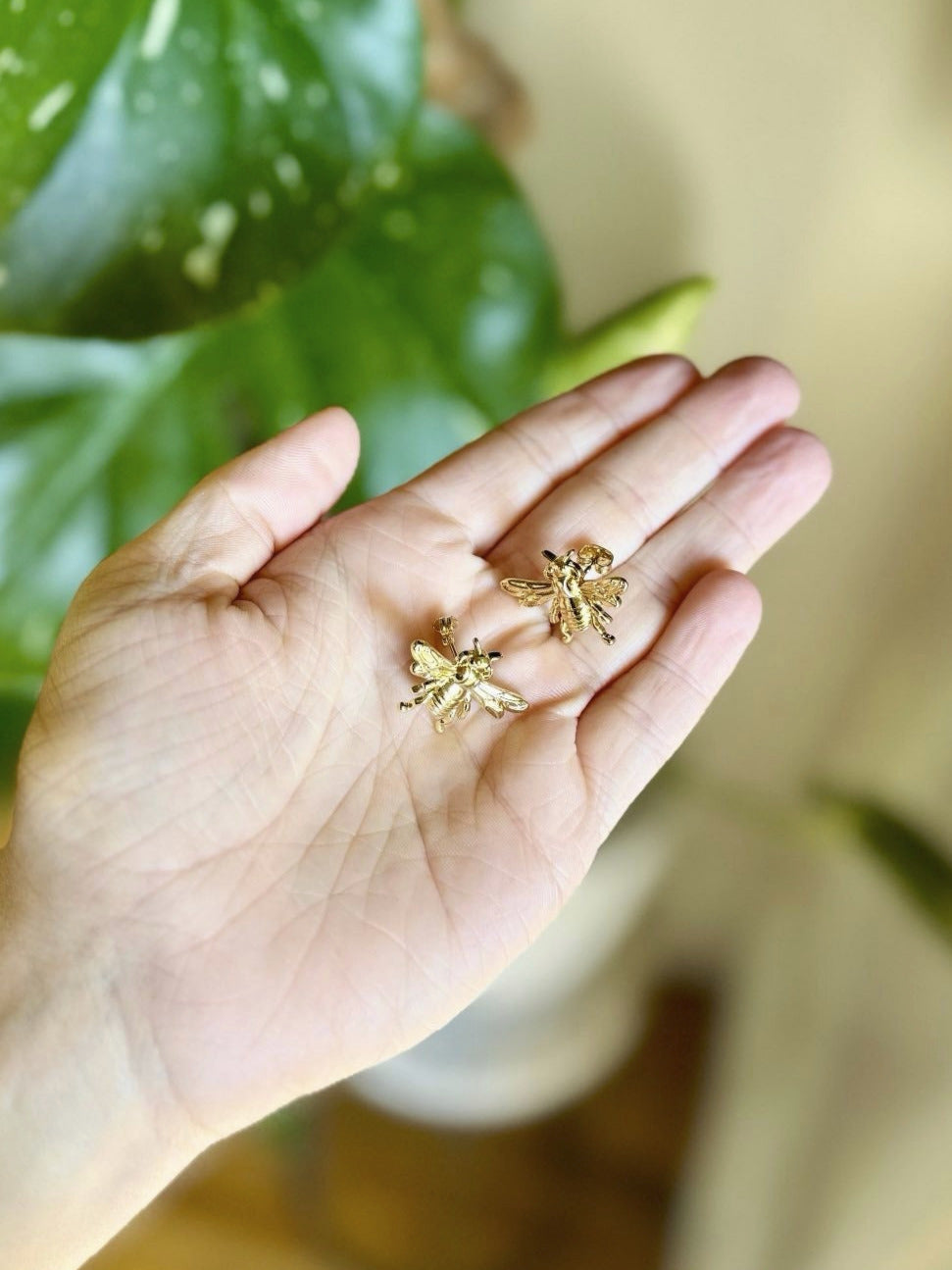Hand holding gold earrings with a blurred green plant in the background