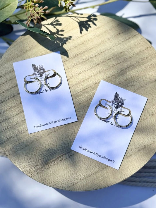 Pair of silver earrings on cards with greenery in the background