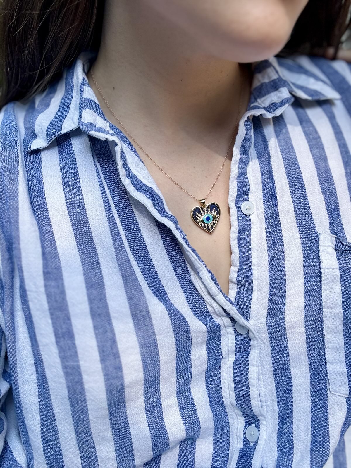 Person wearing a blue and white striped shirt with a necklace featuring a heart-shaped pendant.
