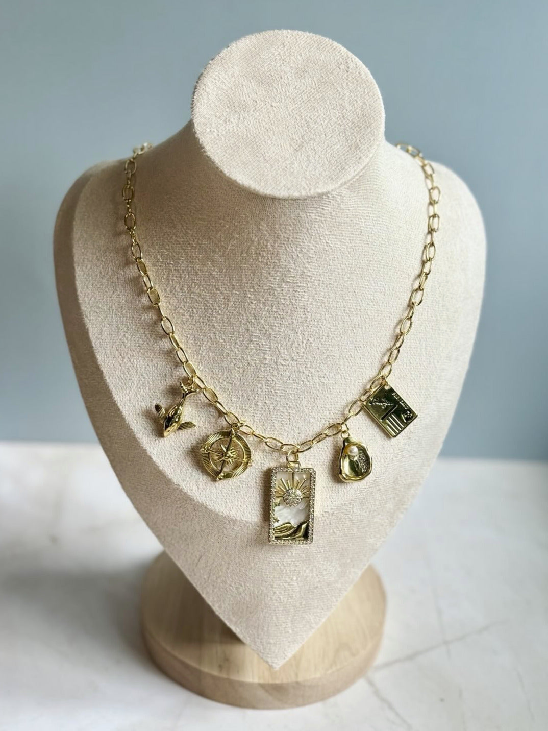 Gold necklace with charms on a mannequin bust against a light blue background