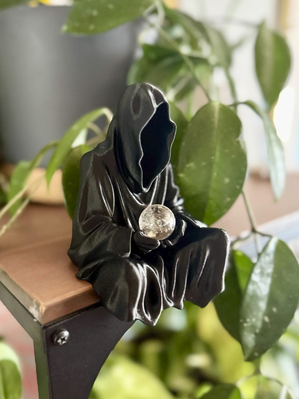 Decorative metal bracket with a black finish on a plant stand, surrounded by greenery.
