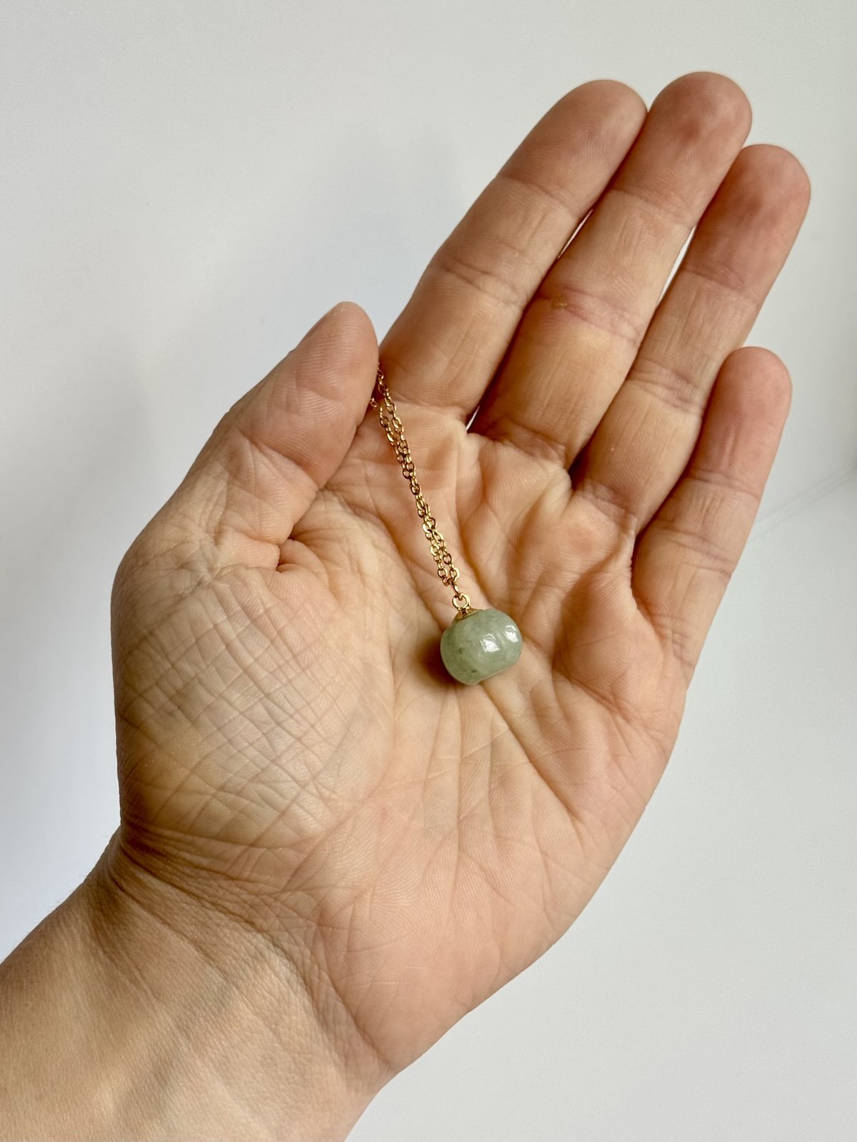 Hand holding a necklace with a green bead against a plain background