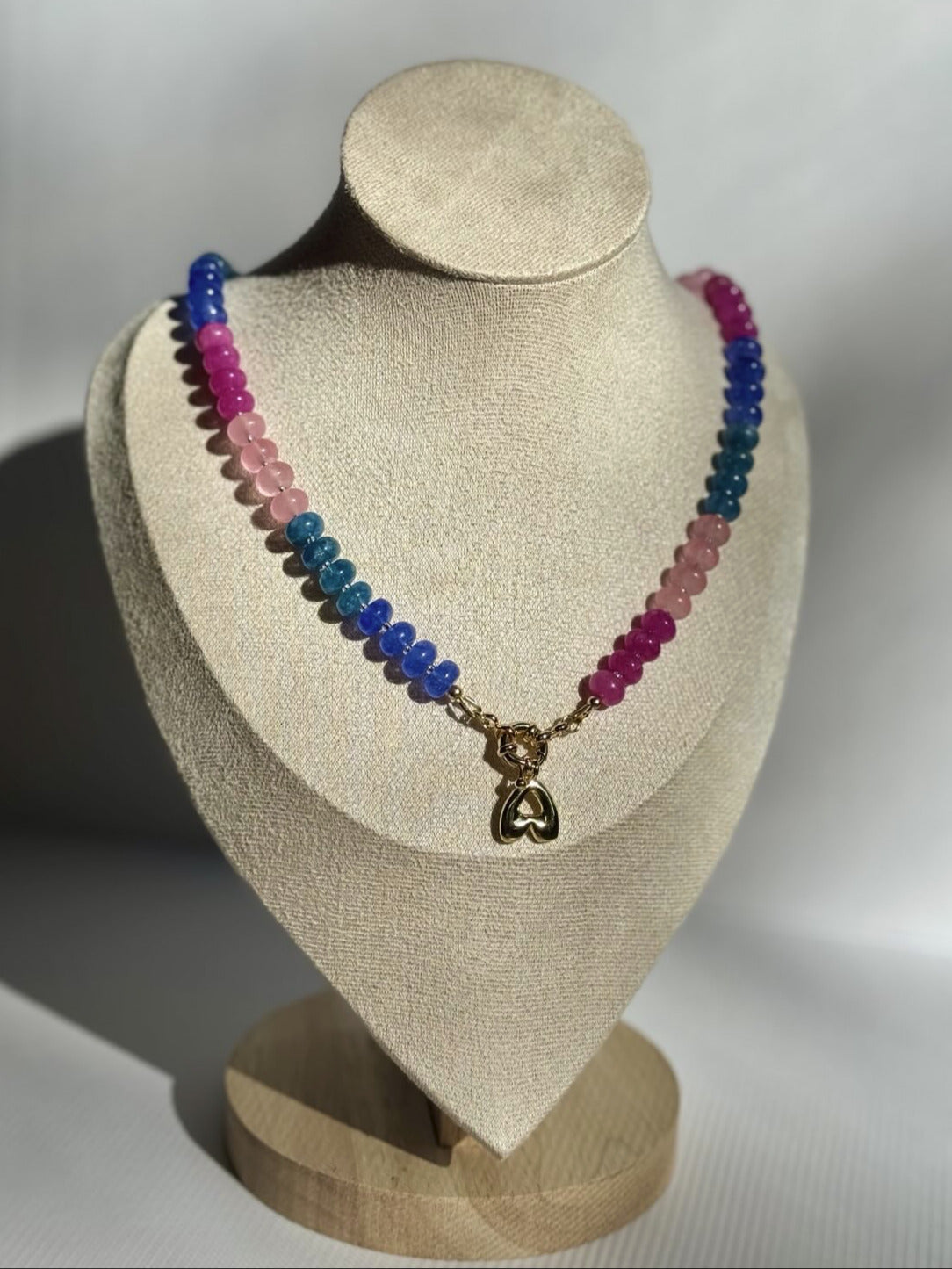 Necklace with multicolored beads and a heart pendant on a beige bust