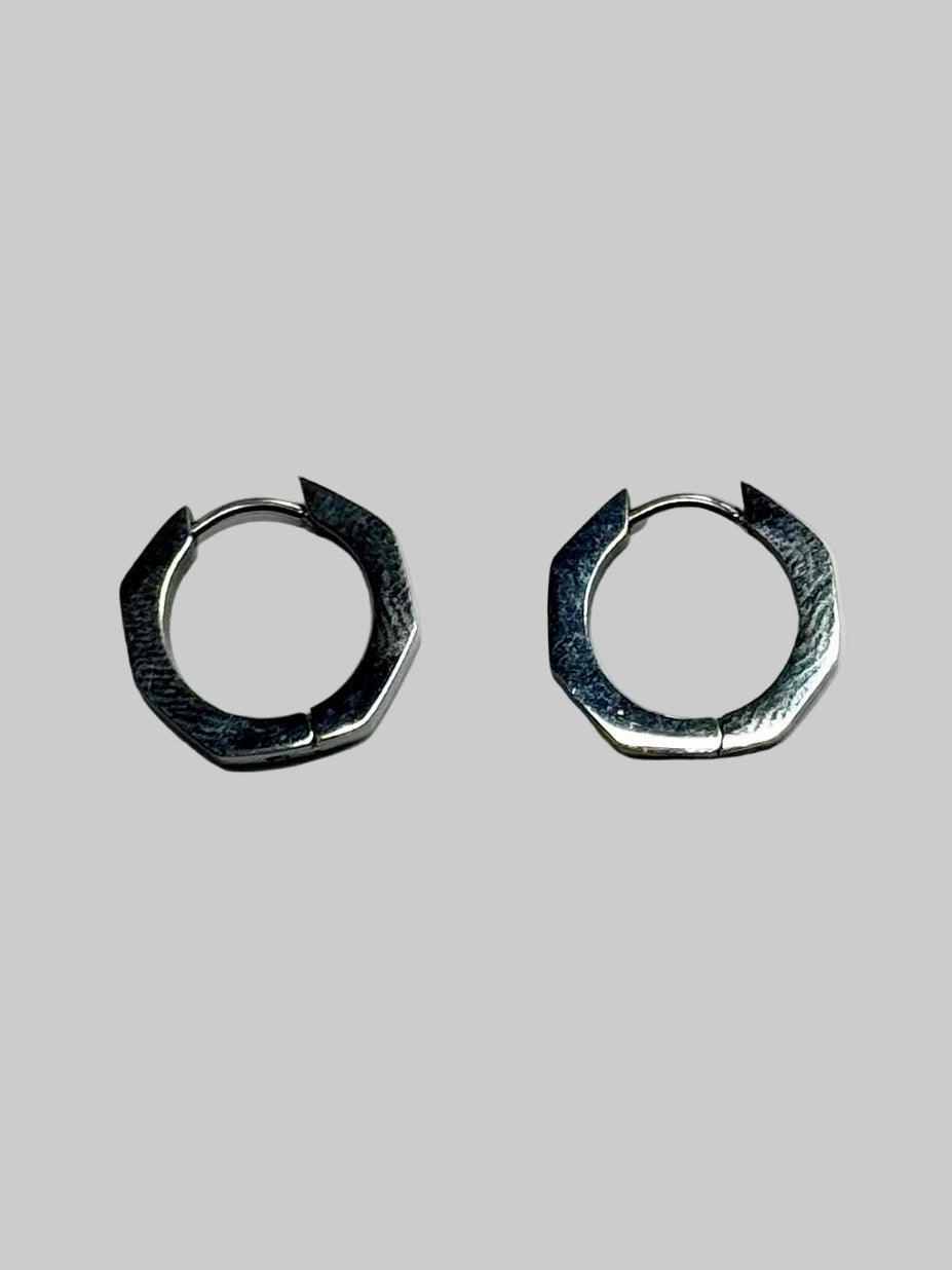 Pair of silver hexagonal hoop earrings on a light gray background