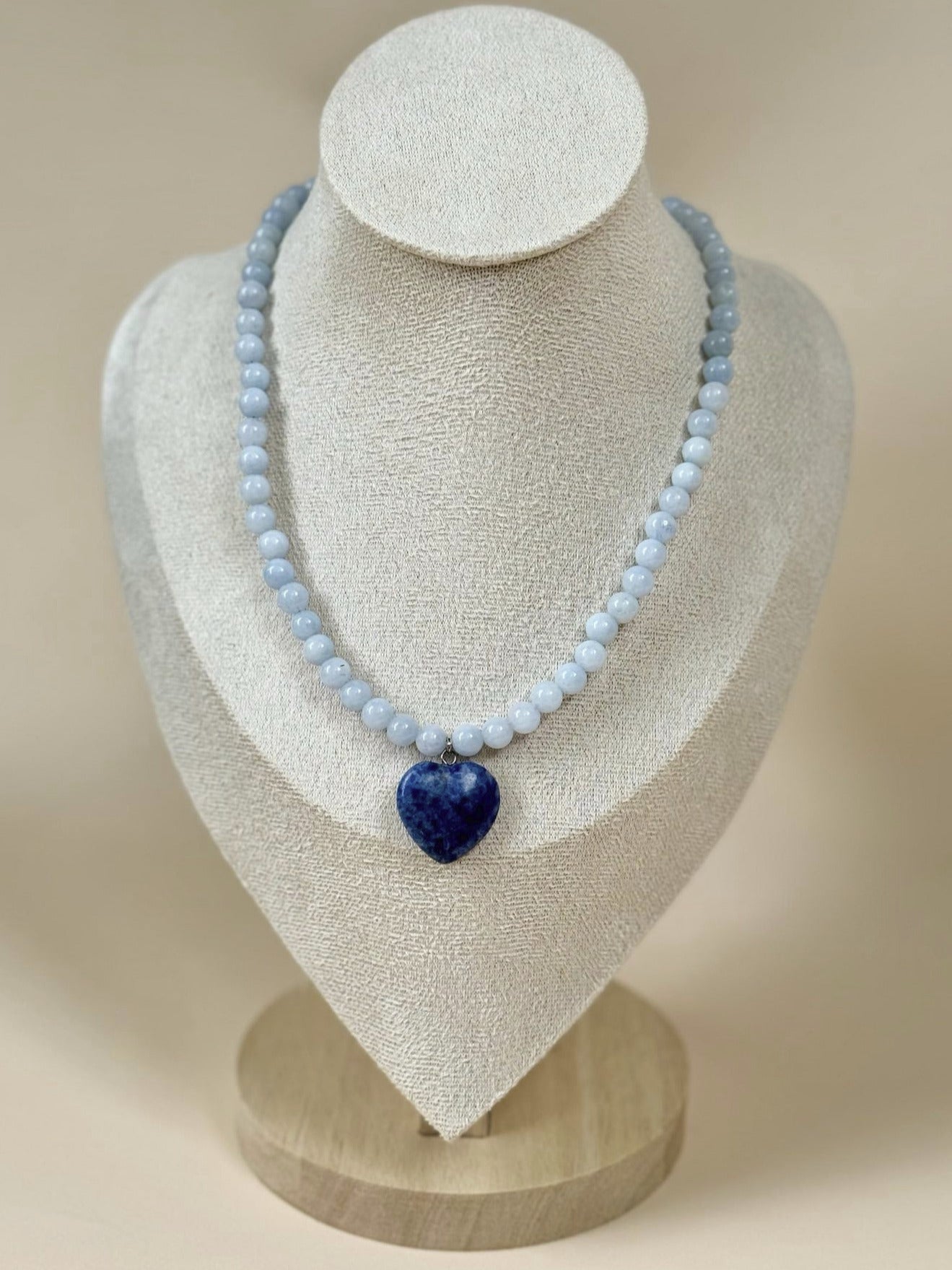 Necklace with a blue heart pendant on a white mannequin bust against a beige background