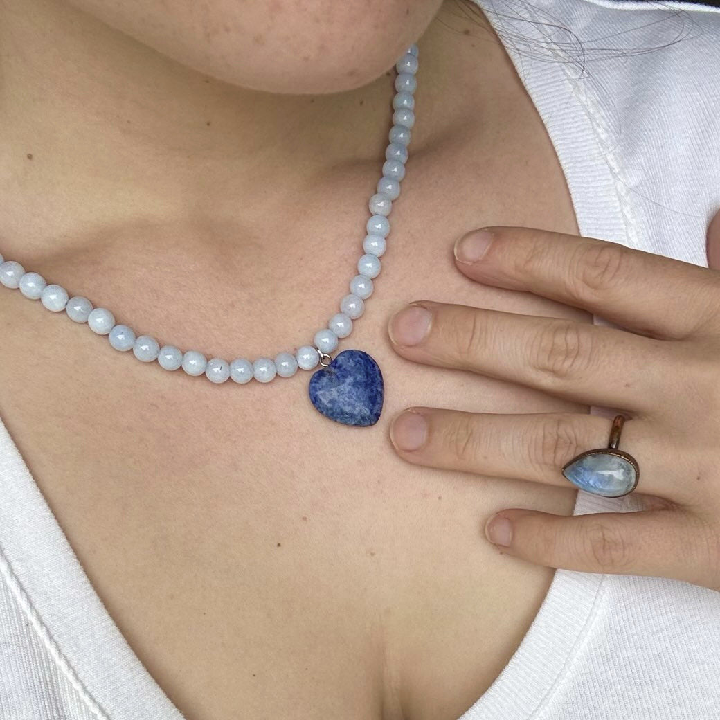 Person wearing a pearl necklace and blue stone ring with a white top.