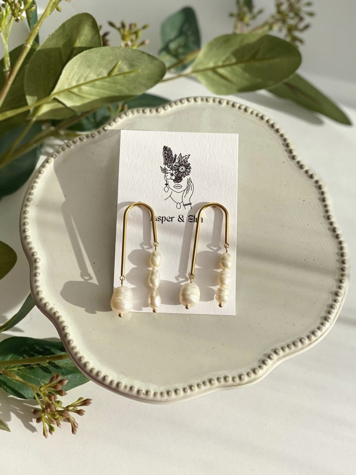 Gold earrings on a white dish with green leaves in the background