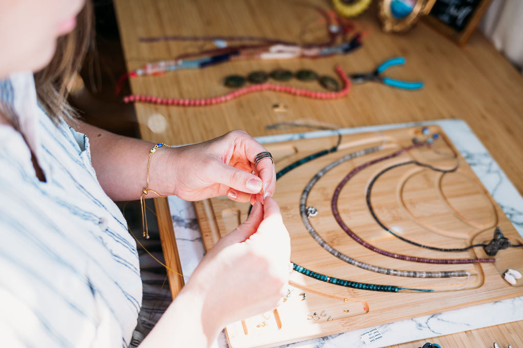 Woman in white striped dress making a pair of earrings at her work bench