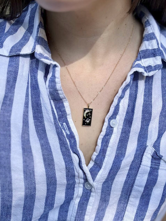 Person wearing a blue and white striped shirt with a necklace featuring a small pendant.
