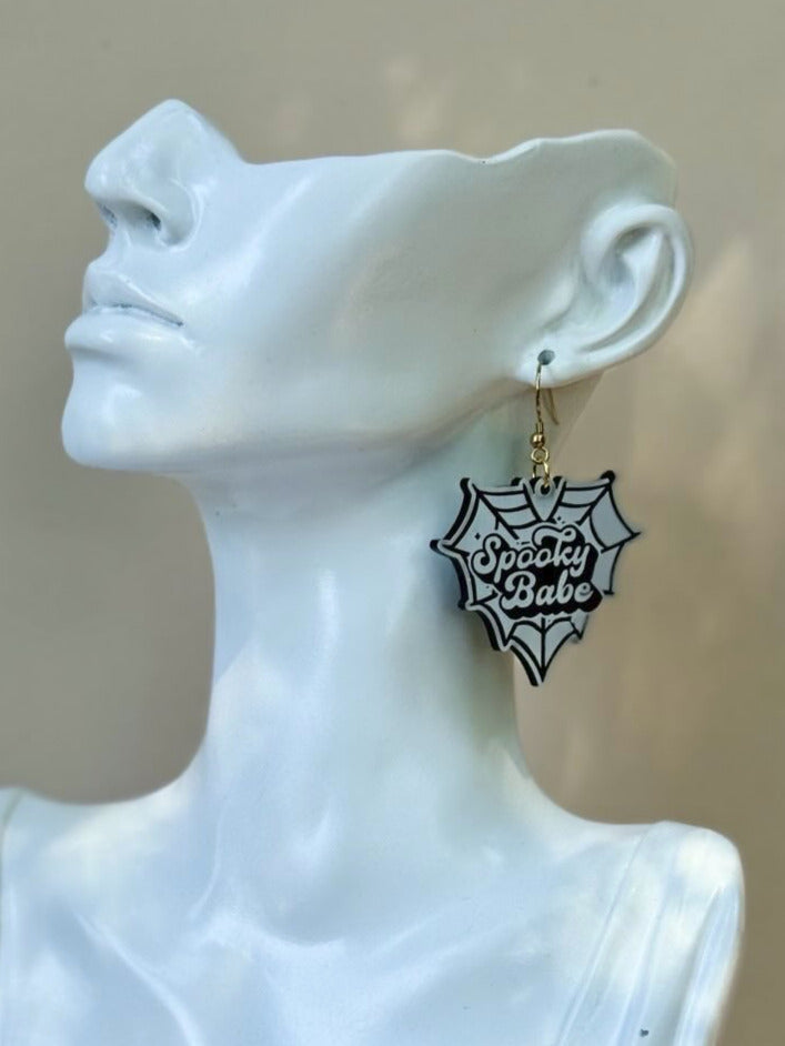 White bust wearing a black and white spider web earring on a neutral background