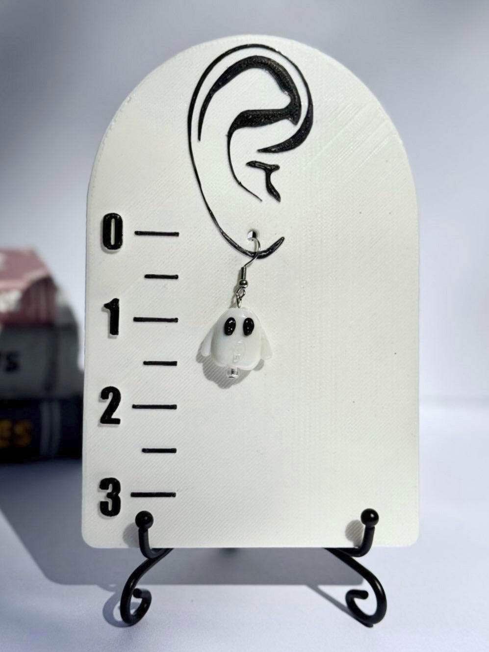 Earring on a measurement scale with a ghost design, against a blurred background.