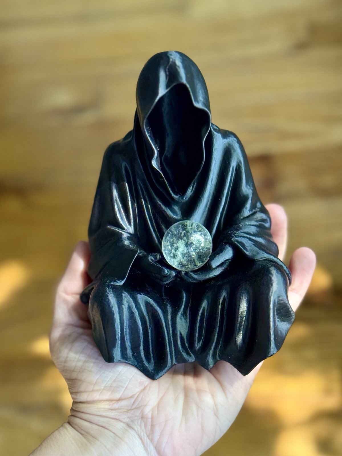 Black hooded figure holding a crystal ball against a blurred wooden background