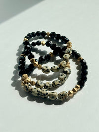 Three beaded bracelets with black, white, and gold beads on a light surface.